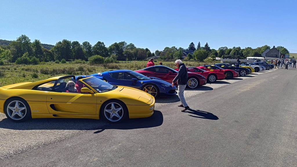 Une rangée de voitures de sport colorées, dont une décapotable jaune au premier plan avec deux personnes à l'intérieur, est garée le long d'une route sous un ciel bleu clair, prête à vivre une expérience inoubliable de supercarstour. porsche auvergne