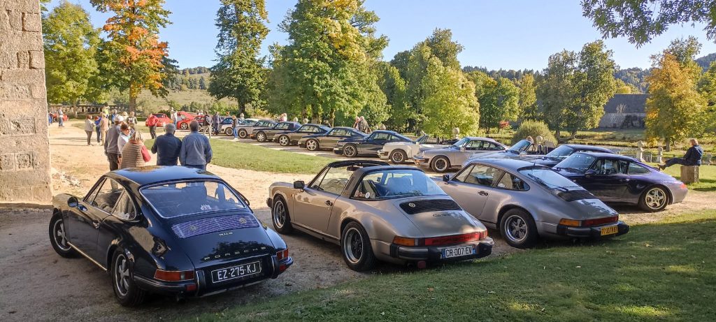 Un groupe de voitures garées sur un terrain, comme si des invités arrivaient pour une fête de jardin animée. porsche auvergne